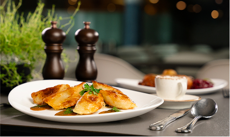 Zrumienione pierogi podane na białym talerzu w otoczeniu ziół i przypraw.